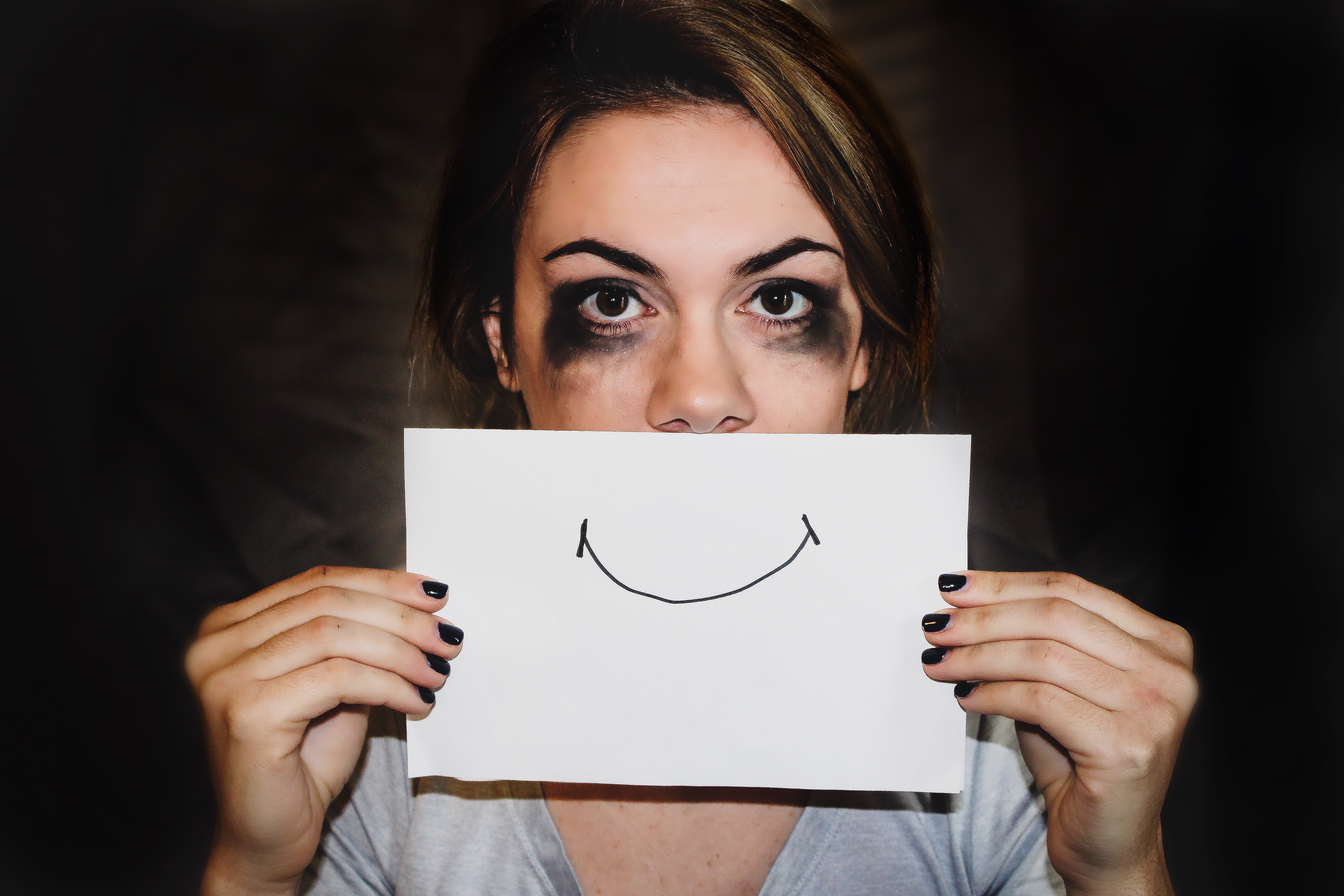 picture is of a woman with a hand drawn smile over her mouth, it looks like she has been crying due to smudged mascara